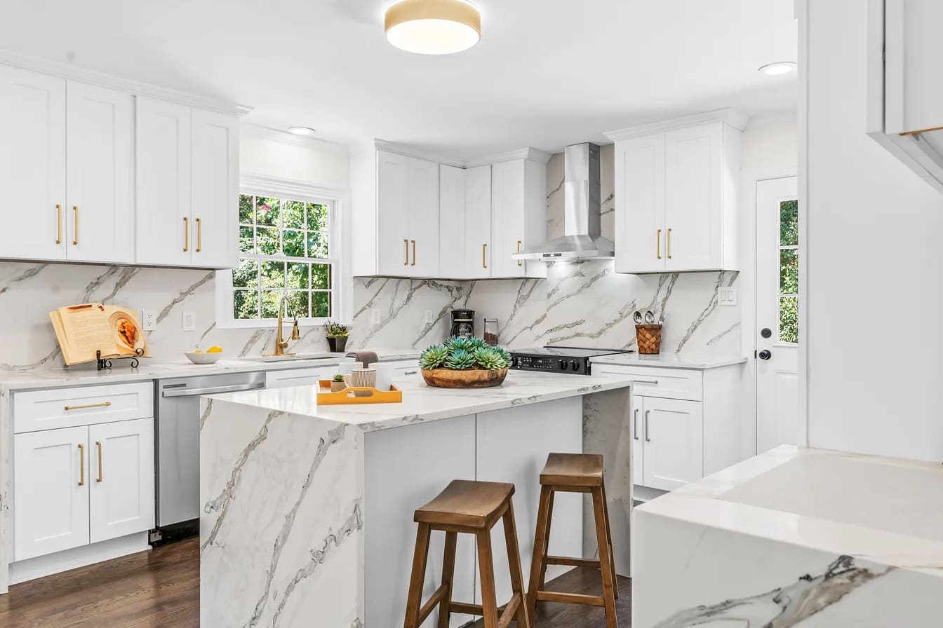 Remodeled kitchen with white shaker cabinets, brass hardware, and a calacatta quartz island