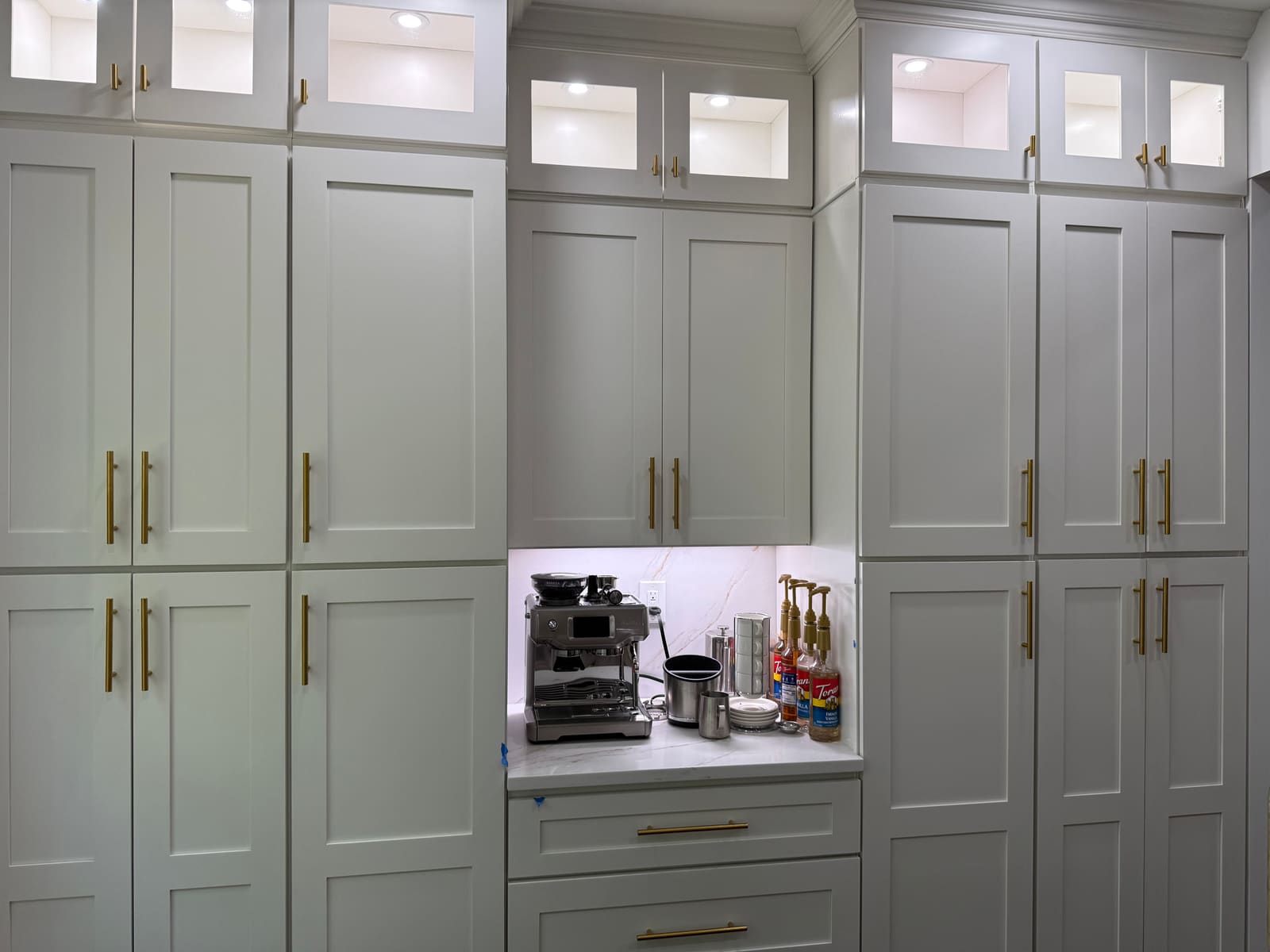 Floor-to-ceiling custom pantry cabinets with lighted glass uppers and coffee nook