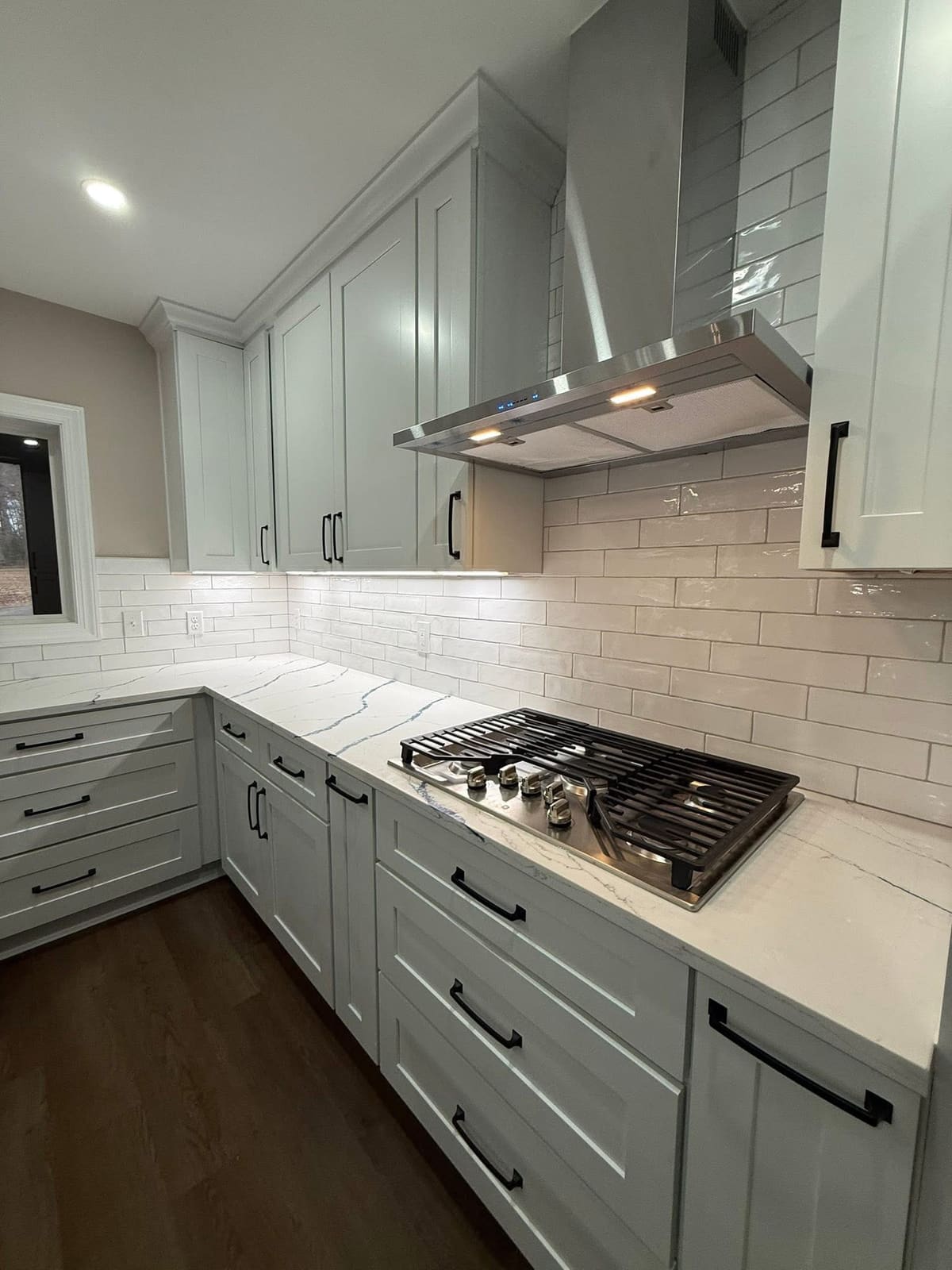 Remodeled kitchen with pale gray-green shaker cabinets, matte black hardware, glossy subway tile, and blue-veined quartz